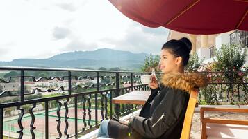 Enjoy the view of the tennis court and distant mountains from this balcony, which offers a comfortable seating area with a table.