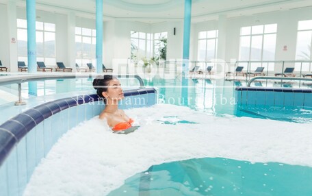 A pool area with lounge chairs and a person in a hot tub.