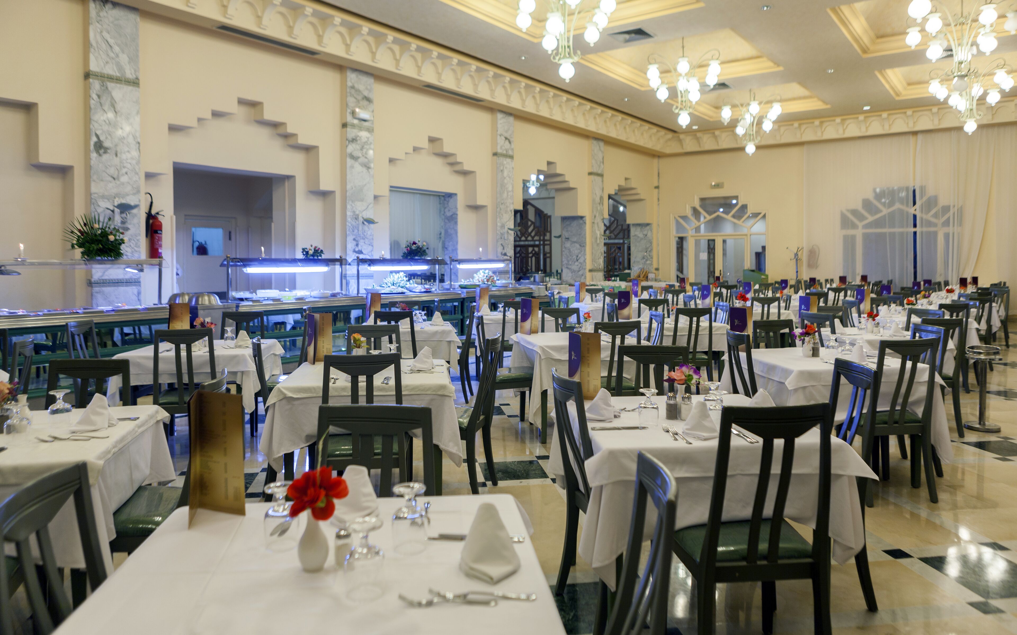 Un comedor formal con varias mesas y sillas, un área central para servir y una iluminación decorativa.