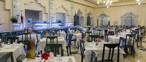 Un comedor formal con varias mesas y sillas, un área central para servir y una iluminación decorativa.