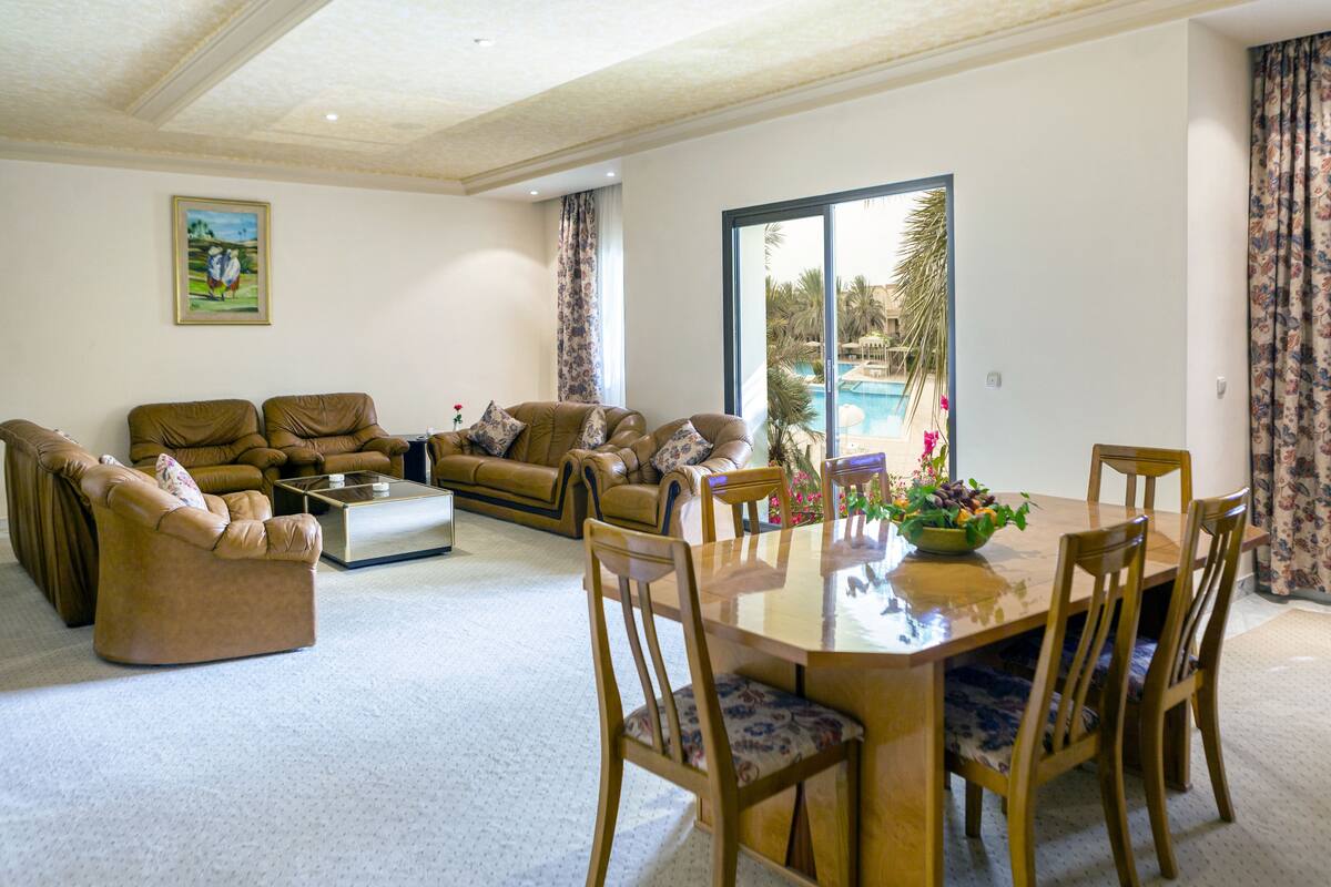 A spacious living room with a large window, a pool view, and a dining area with a table and chairs.