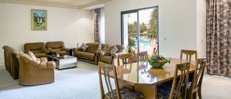 A spacious living room with a large window, a pool view, and a dining area with a table and chairs.