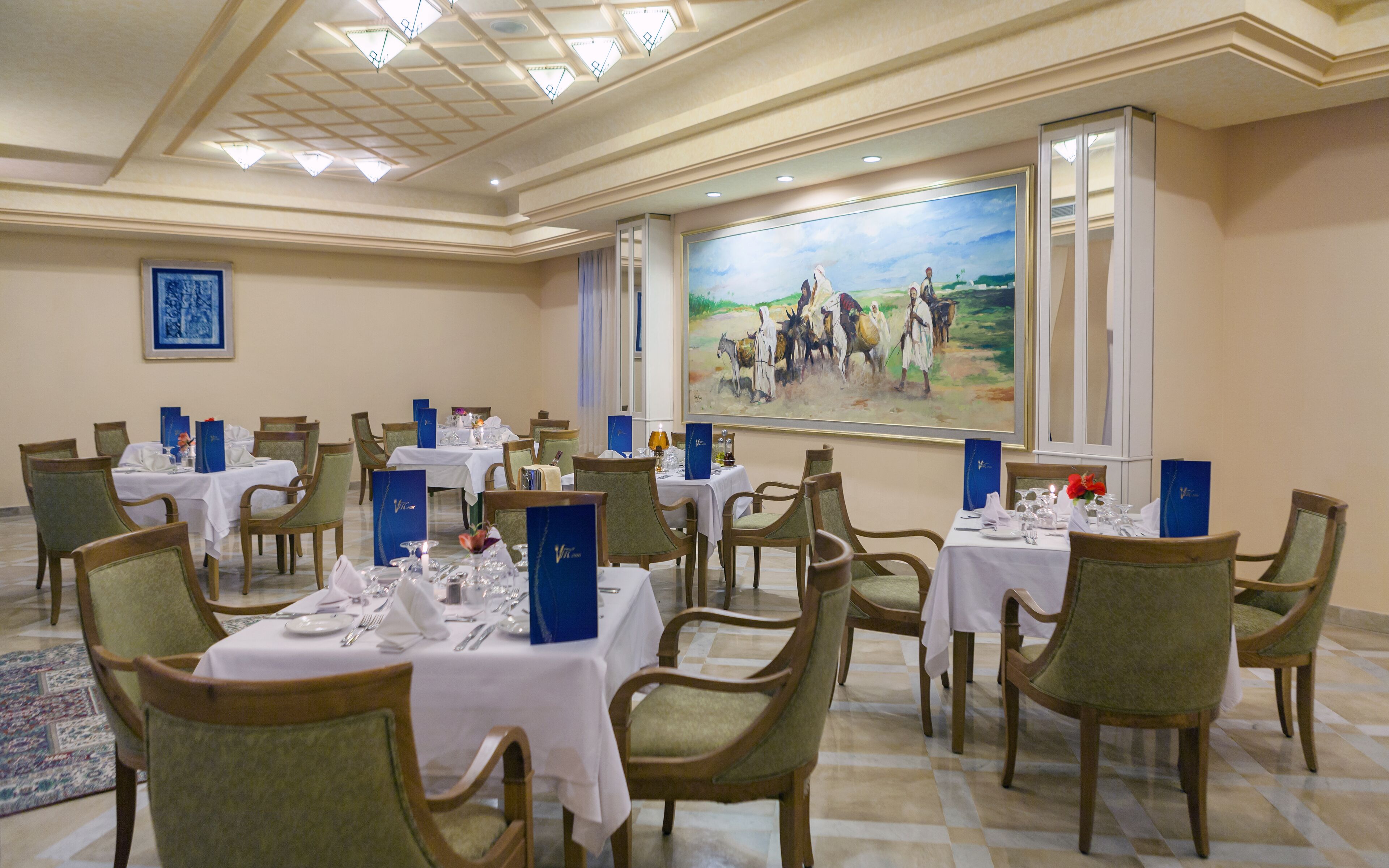 A dining area with multiple tables set for service, chairs, and a large painting on the wall.