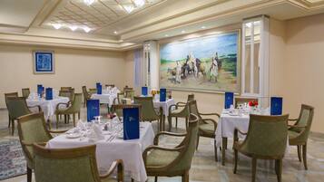 A dining area with multiple tables set for service, chairs, and a large painting on the wall.