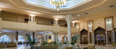A spacious lobby with a high ceiling, a central chandelier, marble flooring, and multiple seating areas.
