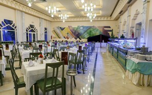 A banquet hall with multiple tables set for dining, a buffet area, and a large mural on the wall. - El Mouradi Douz (Douz Nord)