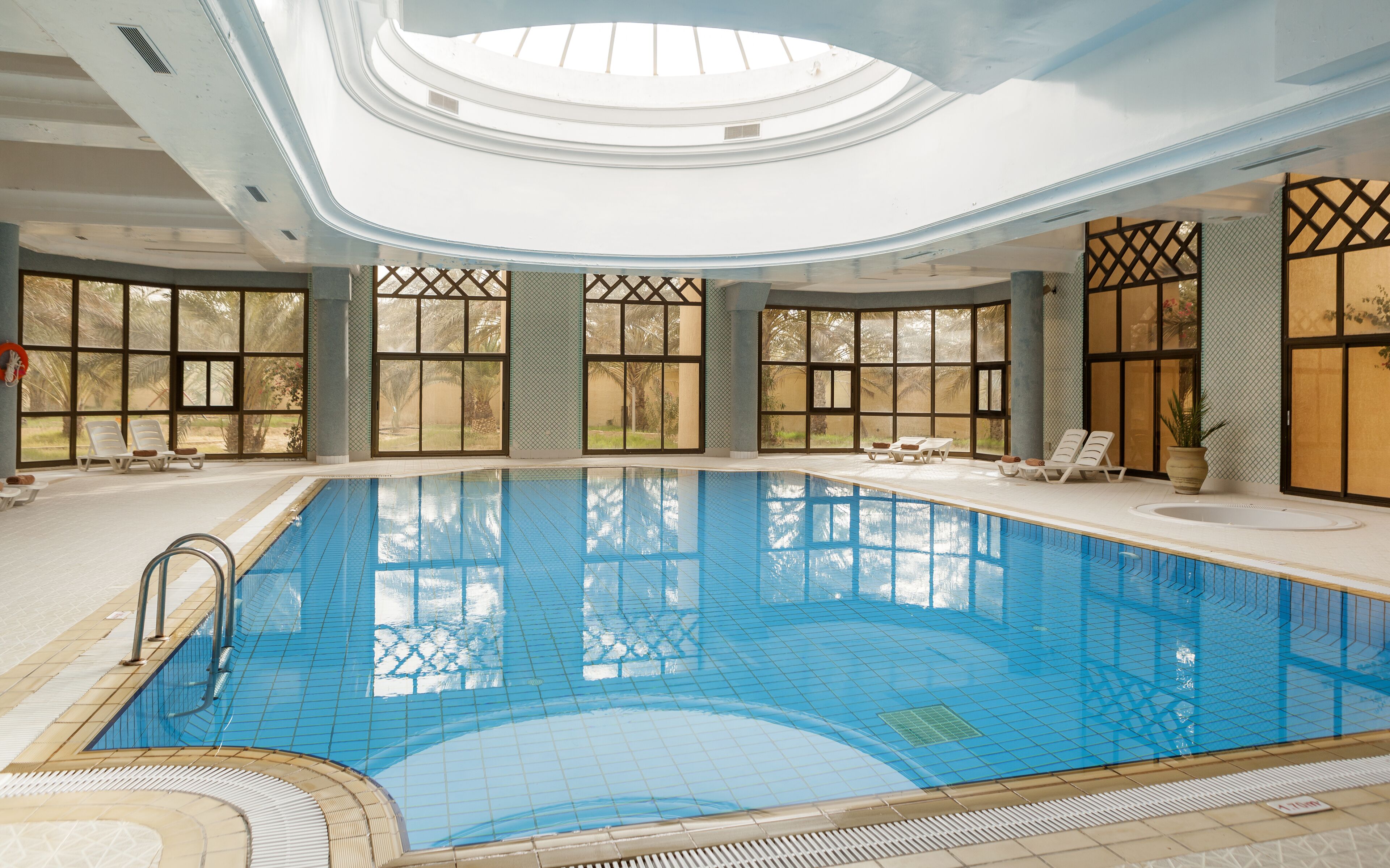 Una piscina interior con paredes de vidrio transparente, sillones de descanso y tragaluces.