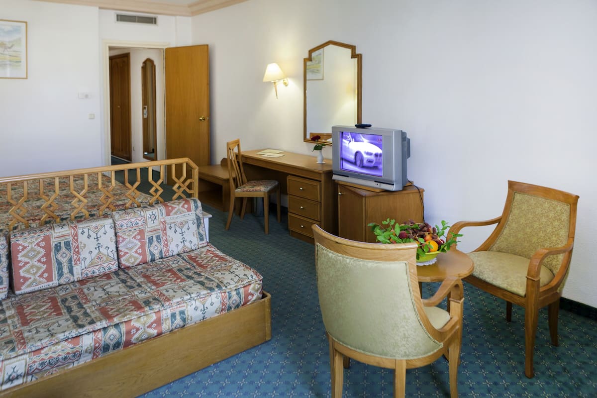 A hotel room with a sofa, a desk with a computer, a chair, a television, and a mirror.