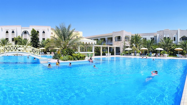 Piscina con un puente, rodeada de palmeras y edificios con balcones.