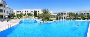 A swimming pool with a bridge, surrounded by palm trees and buildings with balconies. - El Mouradi Douz (Douz Nord)