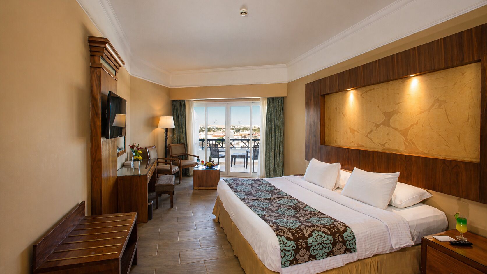 Una camera d'albergo con un letto grande, una scrivania, una sedia, un tavolino e un balcone con tavolo e sedie.