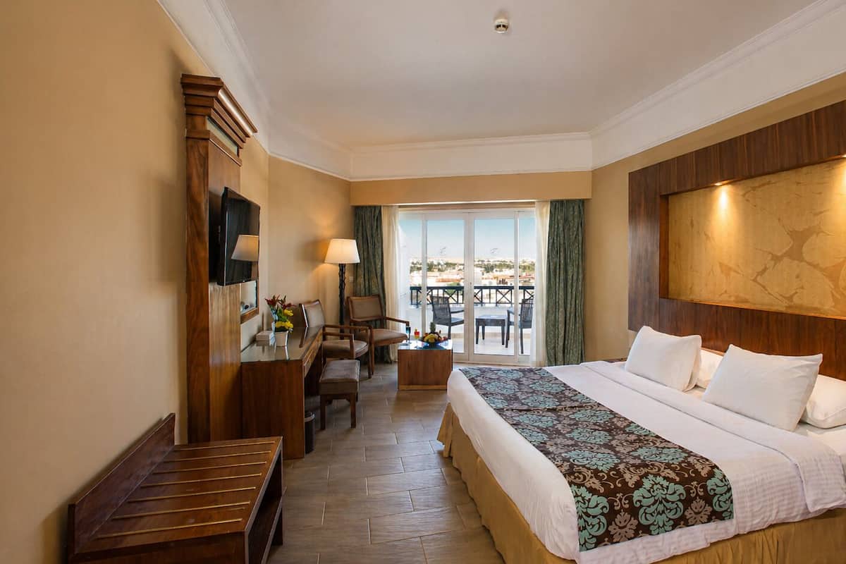 Une chambre d’hôtel avec un grand lit, un bureau, une chaise, une petite table et un balcon équipé d’une table et de chaises.