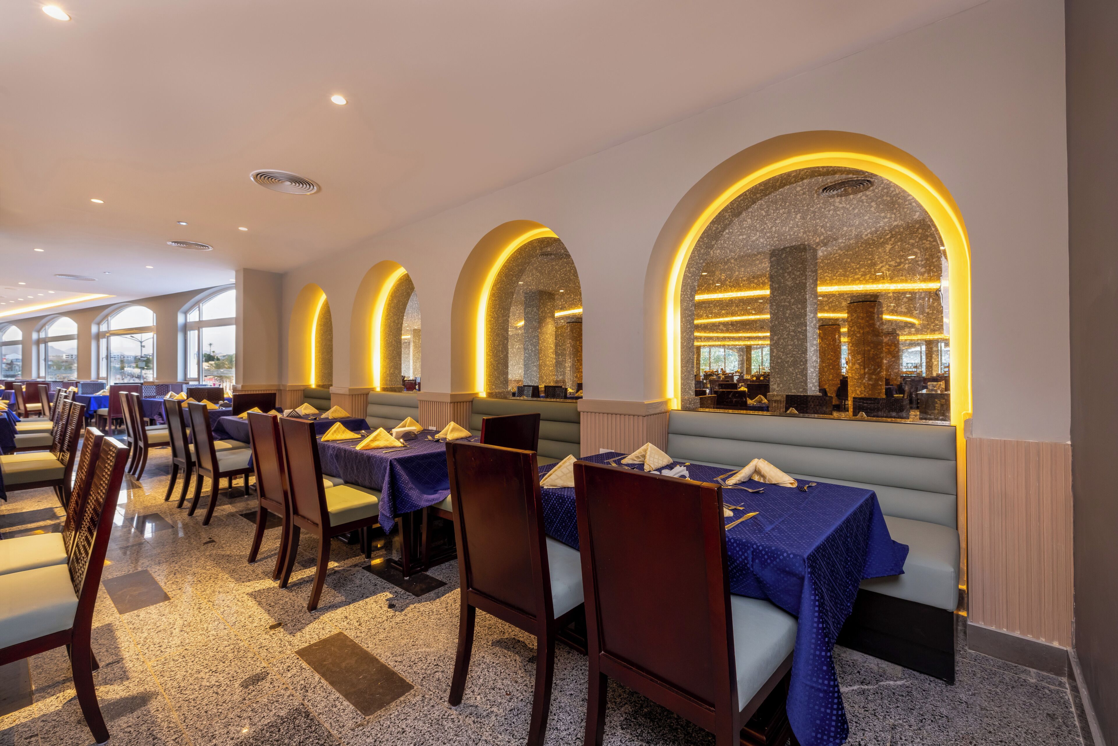 Un restaurant avec des banquettes et des tables, des luminaires en forme d’arc et une vue par les fenêtres.