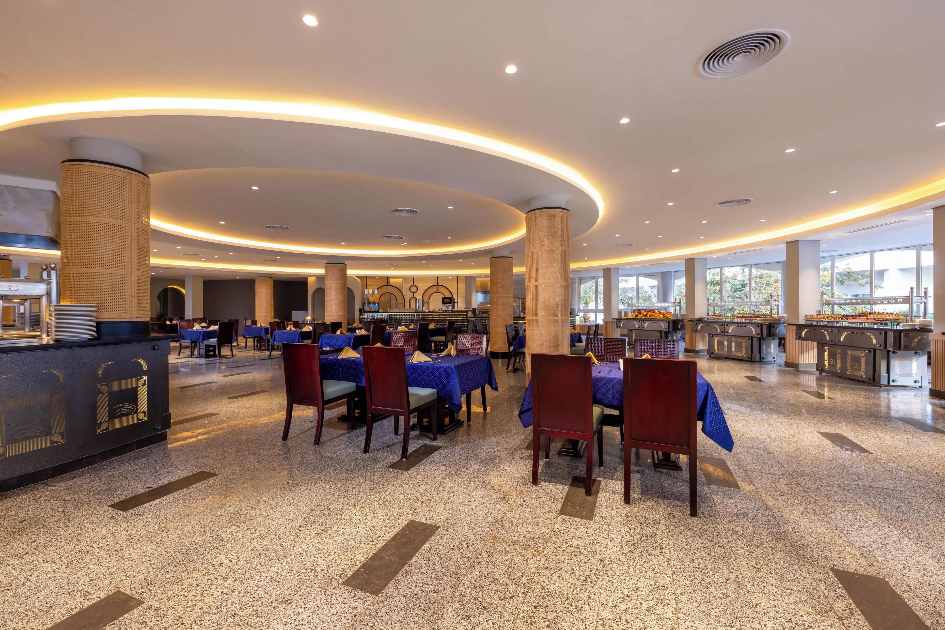 Un vaste espace de restauration d’hôtel, avec des tables rondes, des chaises et un buffet.