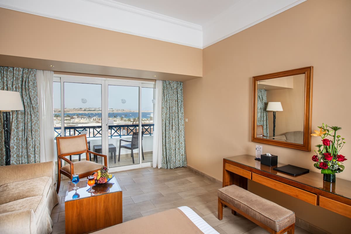 A hotel room with a balcony, a desk, a chair, a sofa, and a bed.
