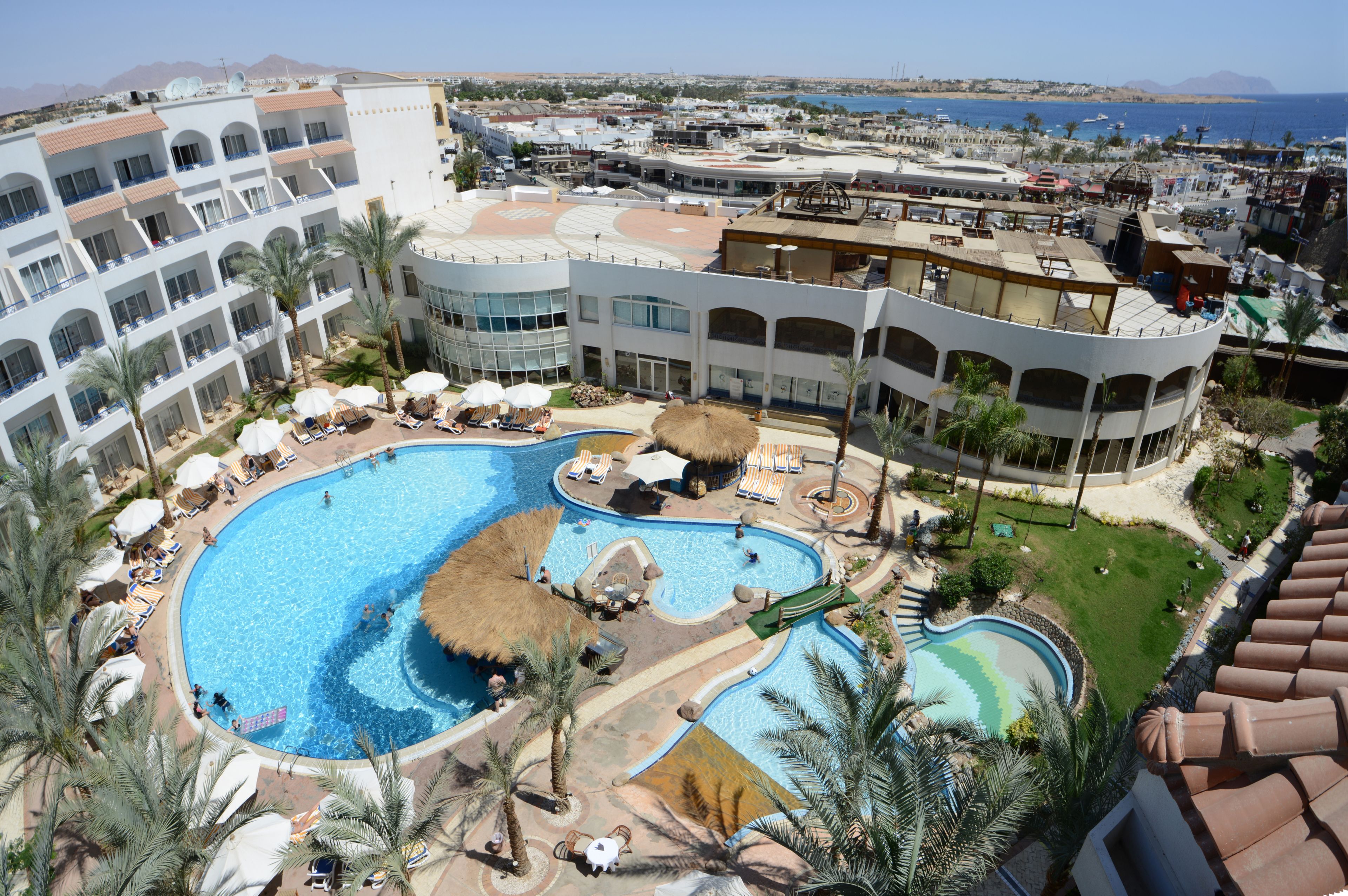 A resort with a large swimming pool, sun loungers, and a view of the sea.