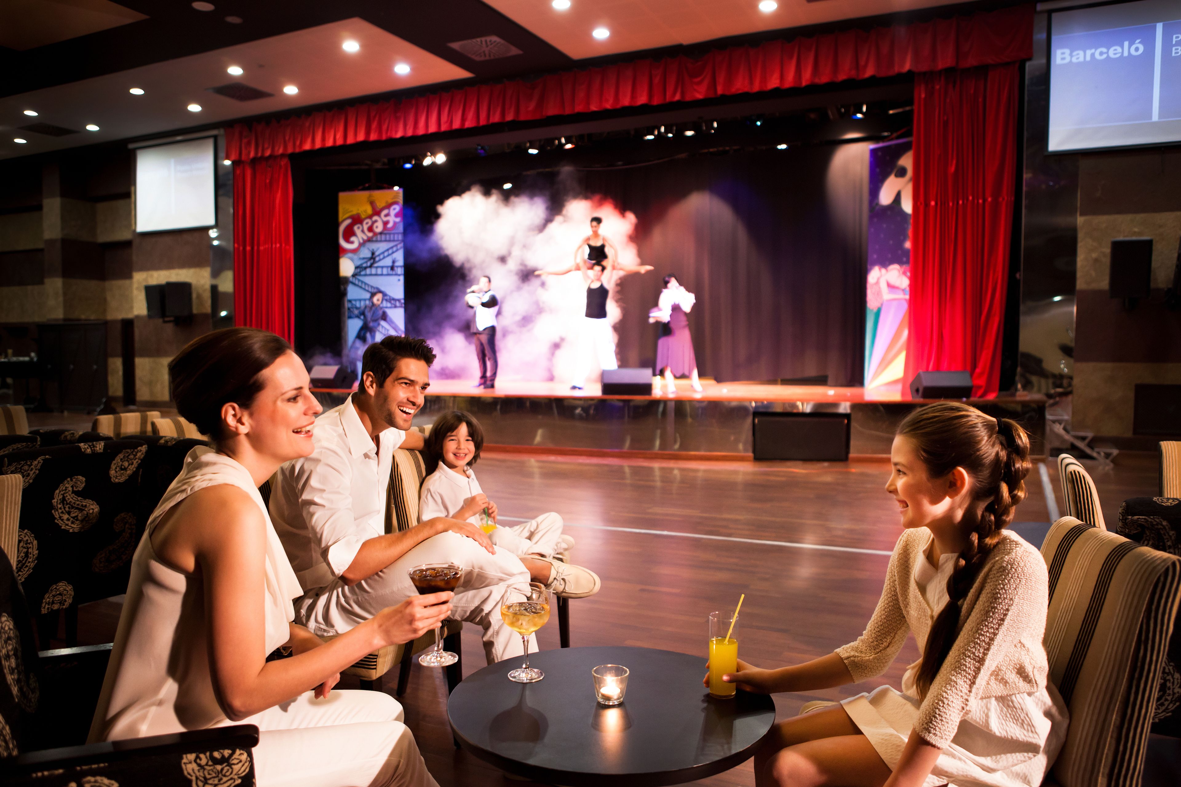 Un grupo de personas sentadas alrededor de una mesa redonda en el vestíbulo de un teatro, con un escenario al fondo.