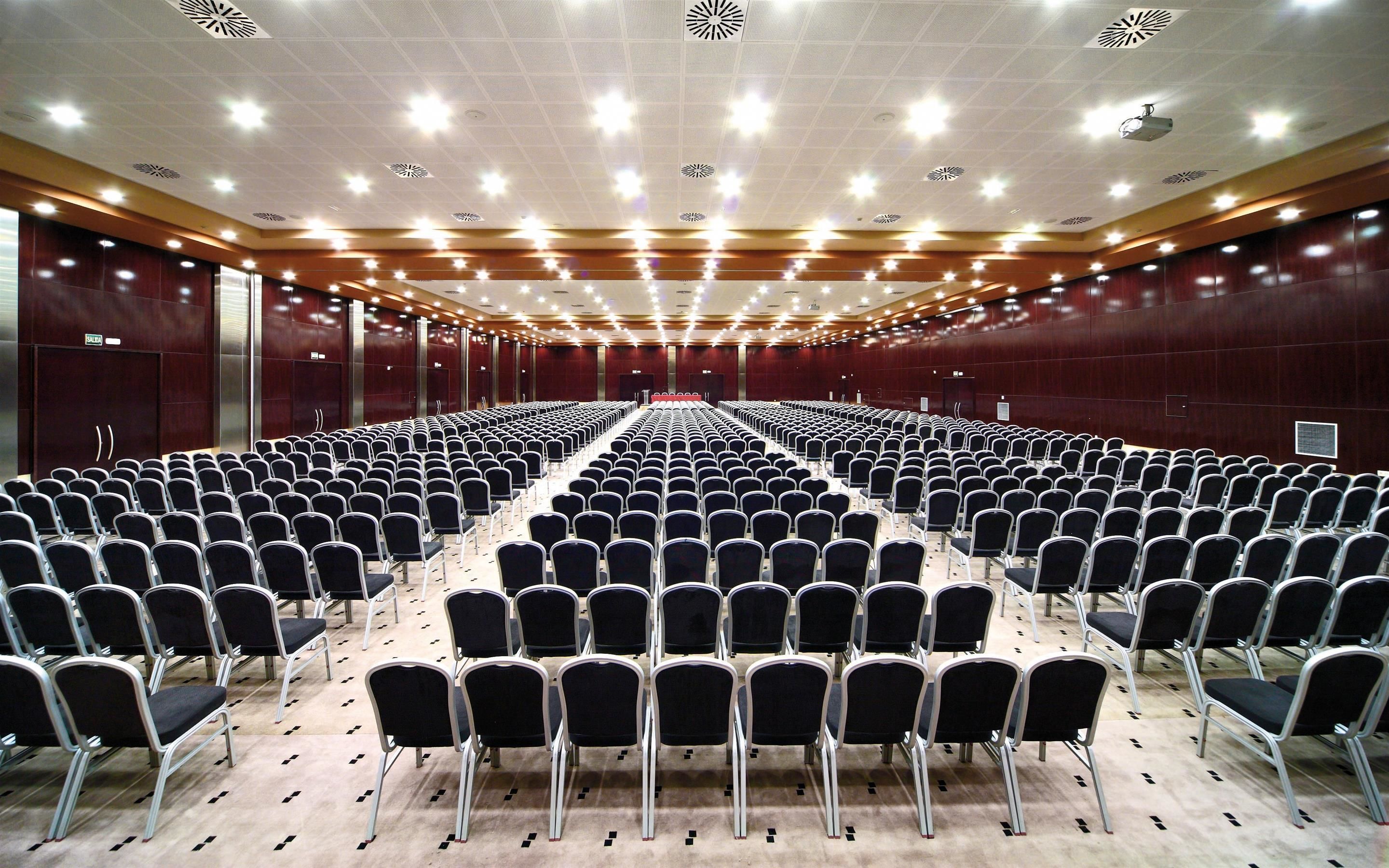 Un amplio salón de conferencias con filas de sillas y un escenario al frente.