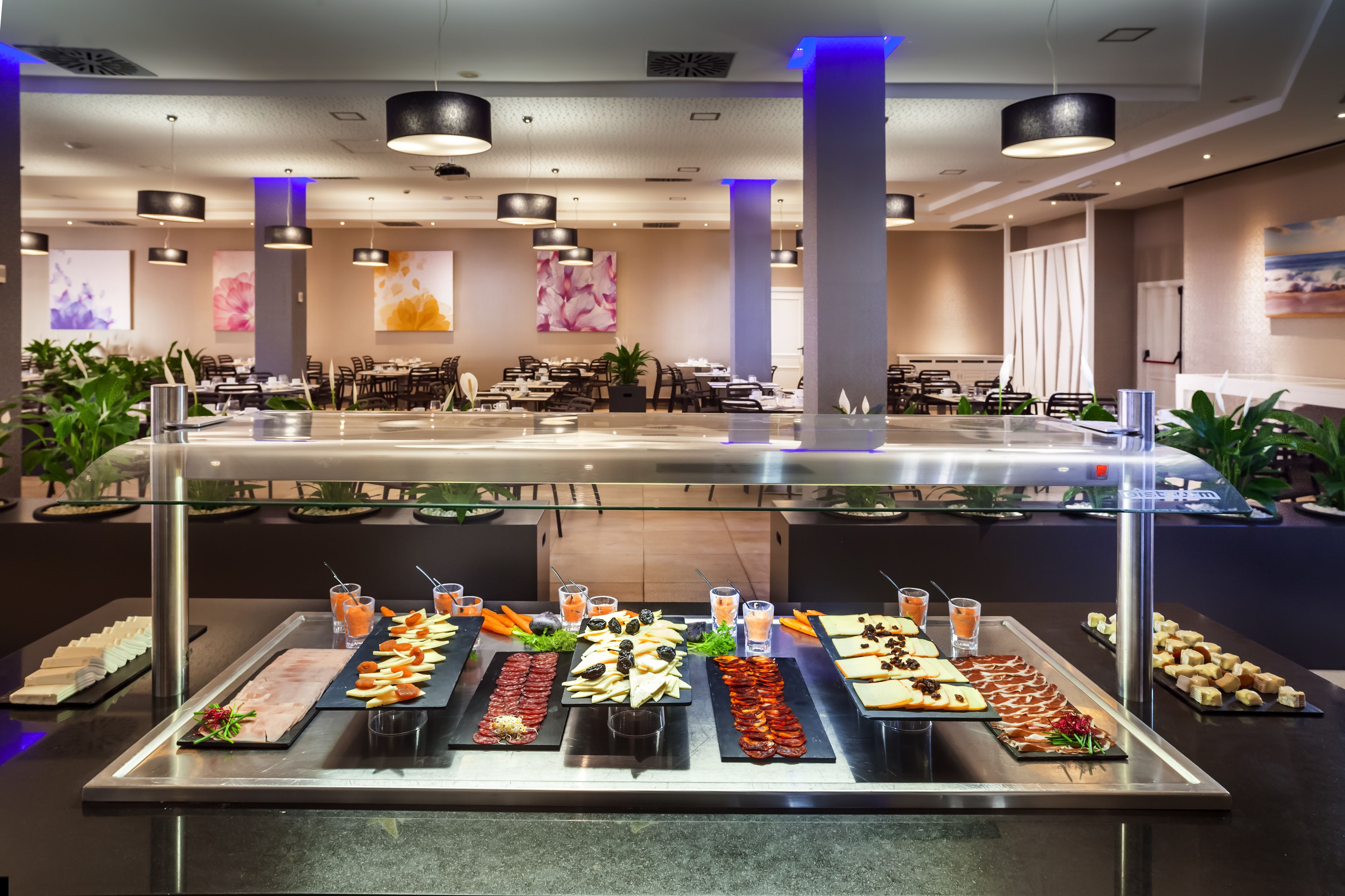 Zona de buffet con diferentes alimentos y bebidas, rodeada de mesas y sillas.