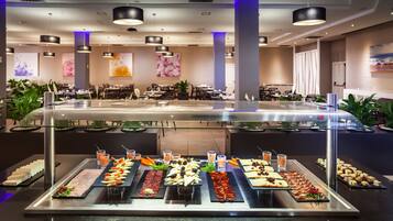 Zona de buffet con diferentes alimentos y bebidas, rodeada de mesas y sillas.