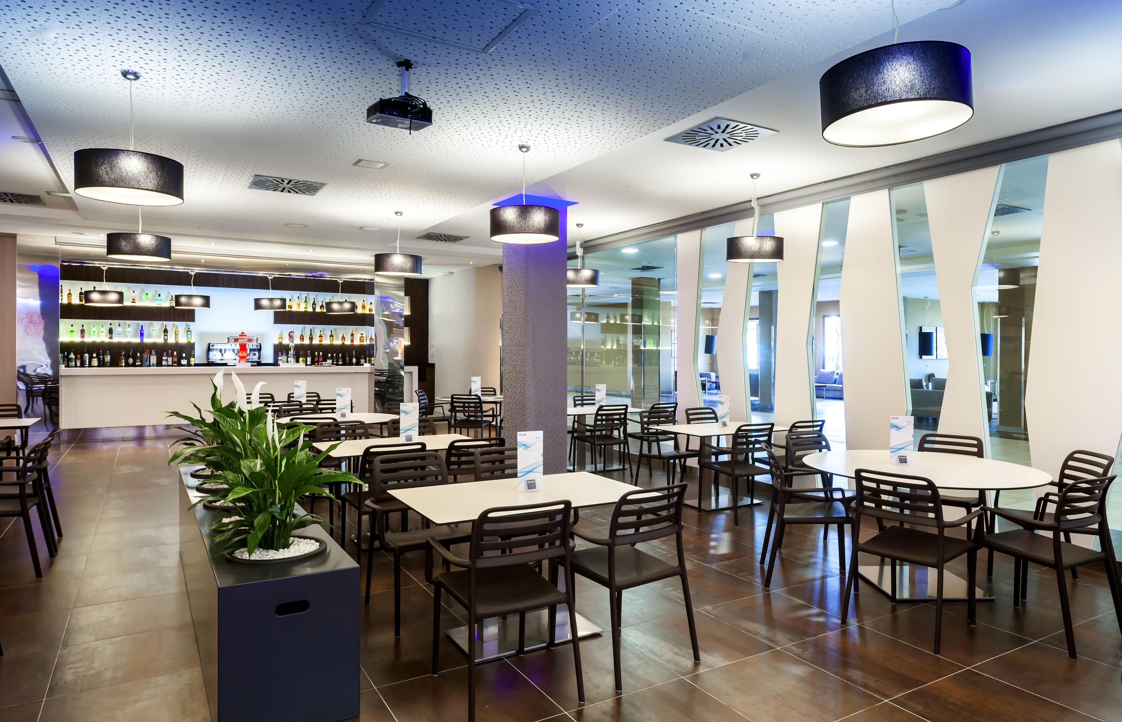 Un restaurante moderno con barra, varias mesas y sillas, y una gran planta en maceta.