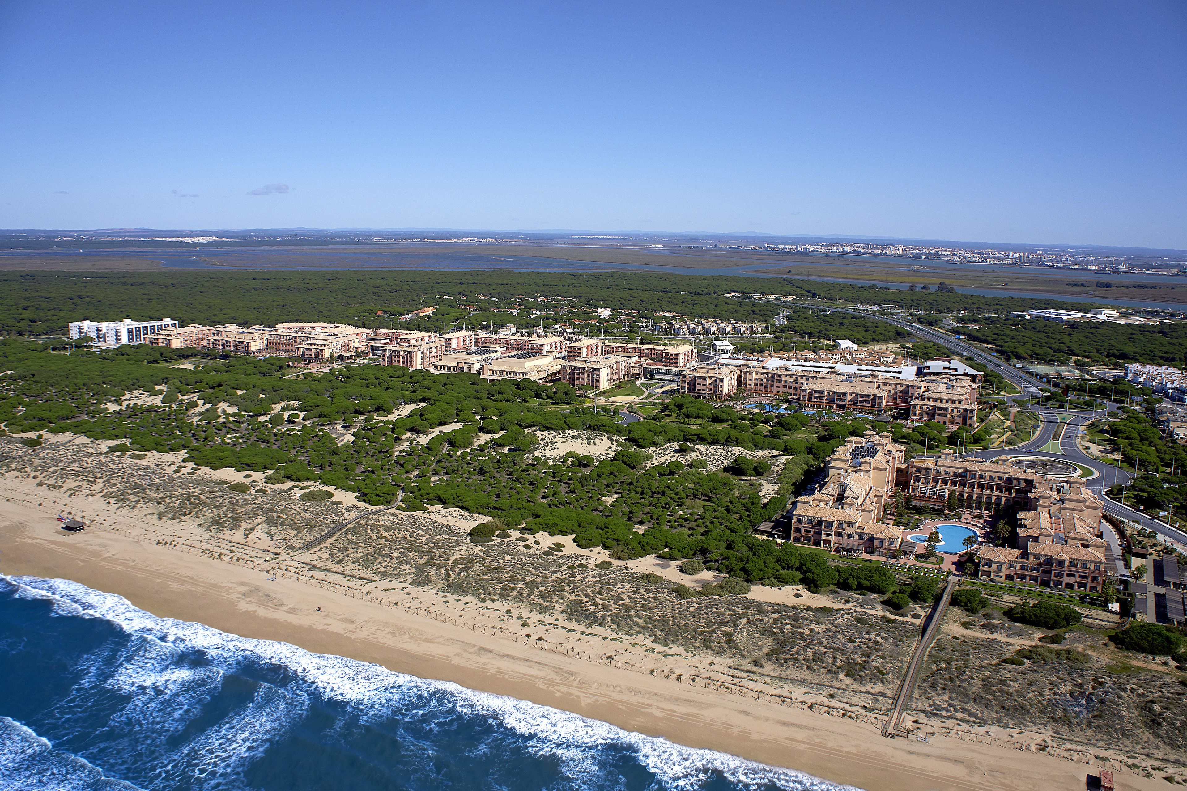 Un resort costero con varias edificaciones, una playa y un camino que conduce a ella.