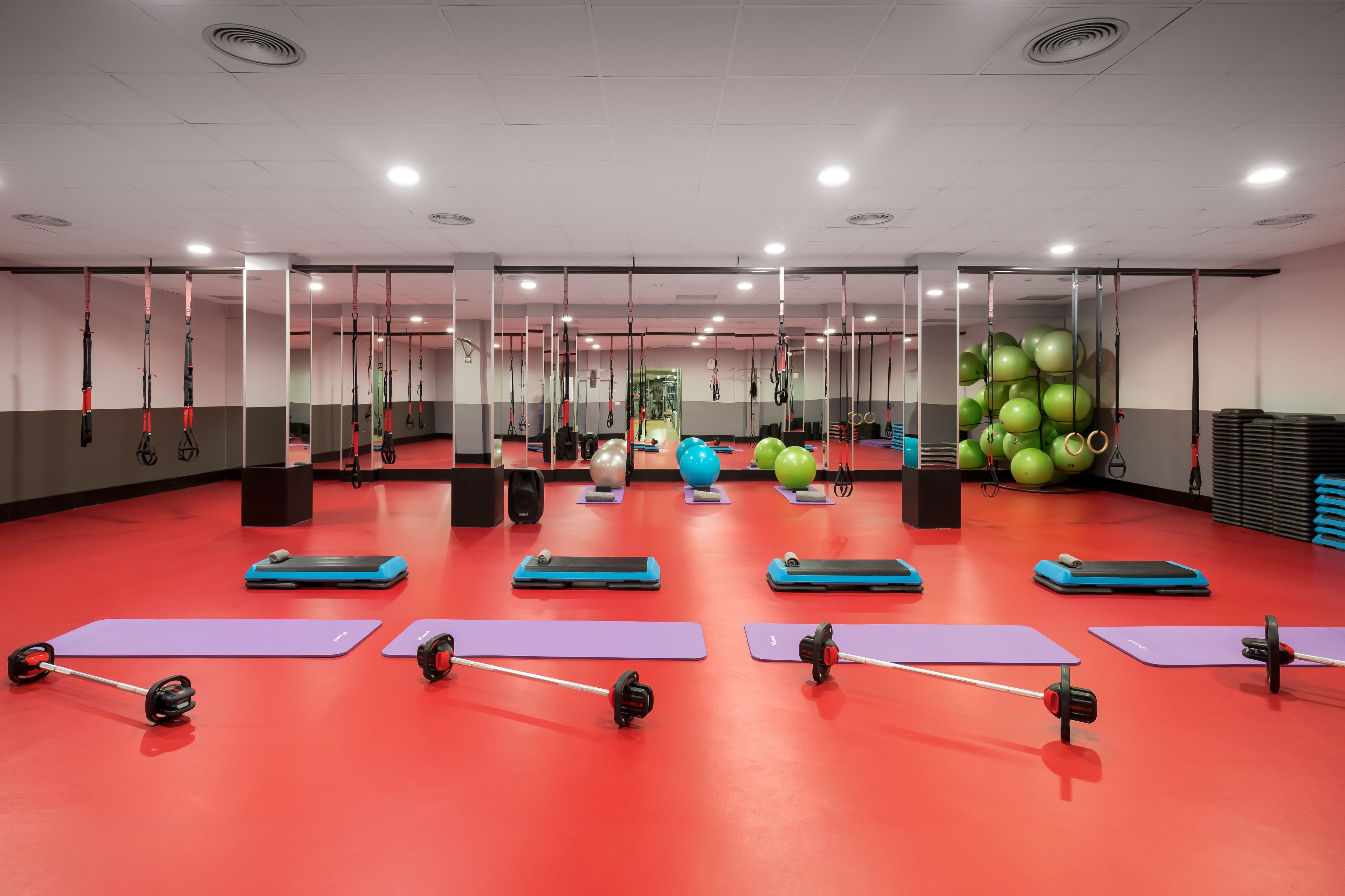A gym with exercise mats, weightlifting equipment, and hanging resistance bands.