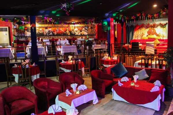A restaurant with red upholstered chairs and tables, a stage with a performer, and festive decorations.