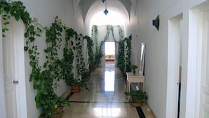 A hallway with a tiled floor, white walls, and green plants on the left. - Rodes (Djerba Midun)