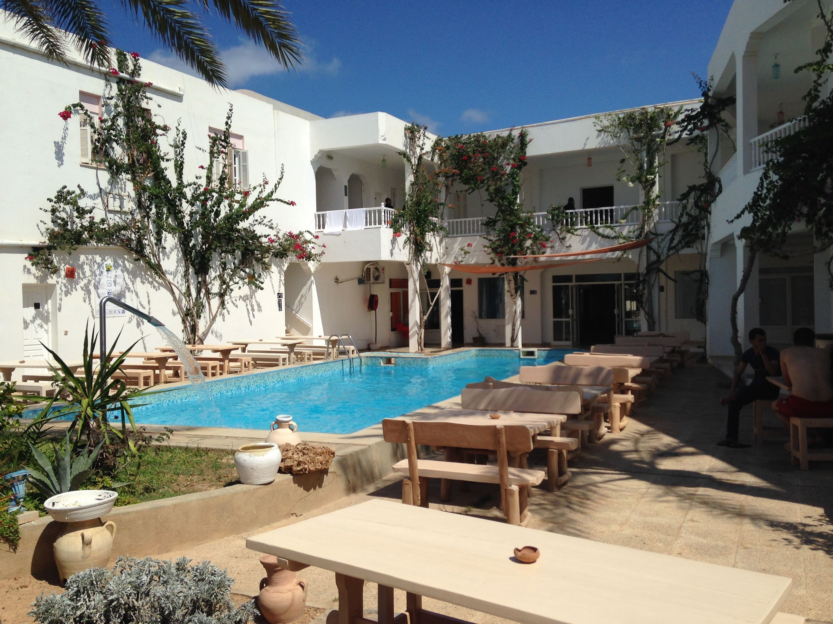 Un espace aménagé au bord de la piscine, avec des chaises longues, une piscine et un bâtiment doté de balcons.