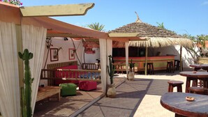 An outdoor patio area with a thatched roof, wooden furniture, and potted plants. - Rodes (Djerba Midun)
