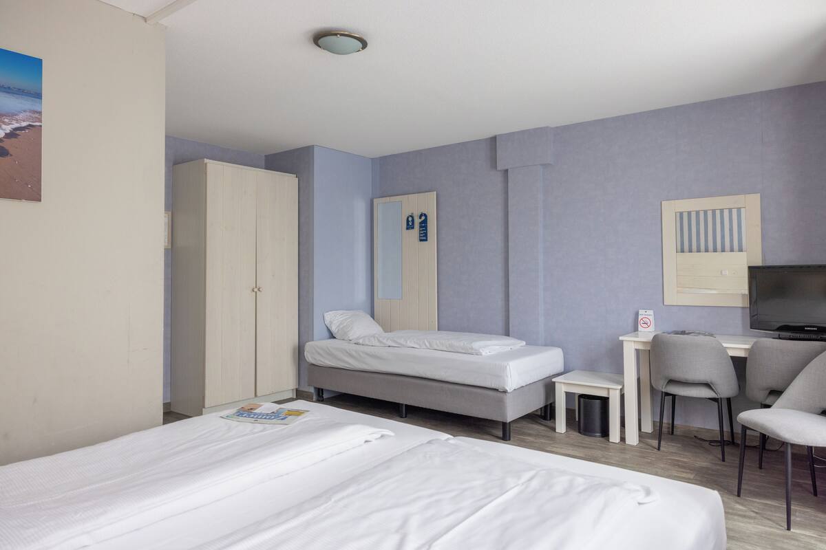 Une chambre d’hôtel avec deux lits, un bureau, une chaise, une télévision et une armoire.