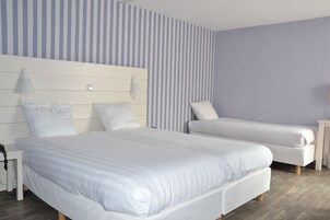 Habitación de hotel con dos camas, una mesita de noche, una lámpara y un papel tapiz a rayas.