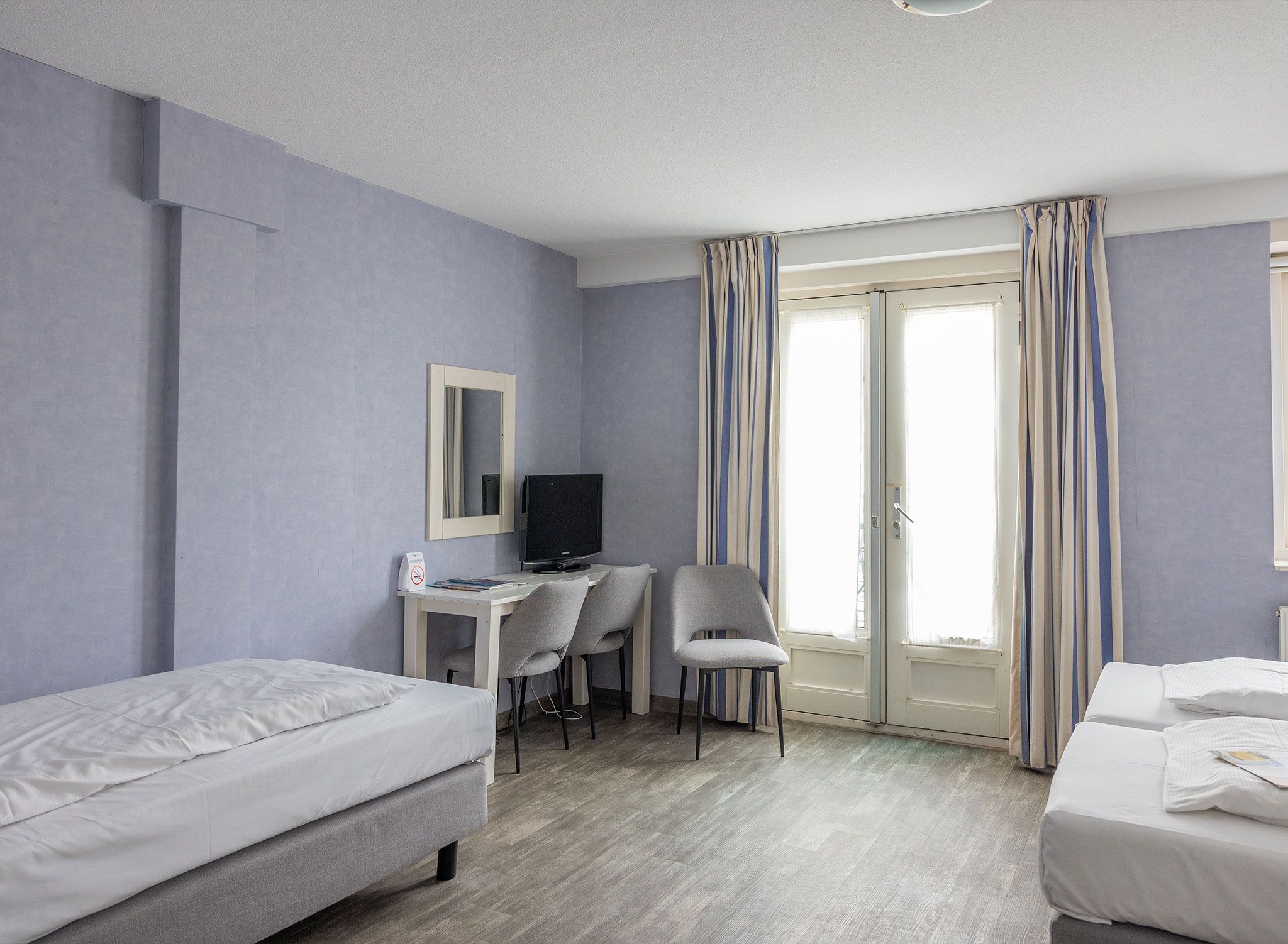 A hotel room with two beds, a desk with a television, and a chair.