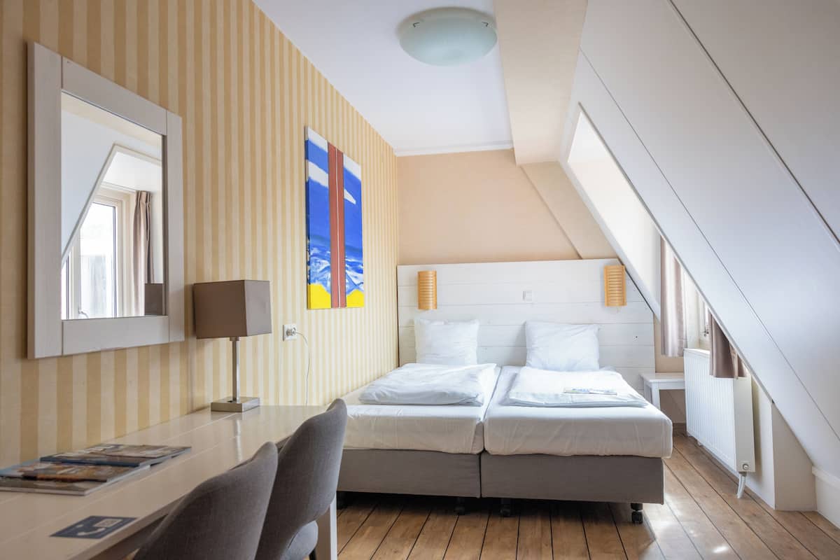 Une chambre d’hôtel avec un lit, un bureau, une chaise, une lampe et une fenêtre.