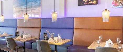 Ein Restaurantinneres mit Sitzecken, Tischen und hängenden Pendelleuchten.