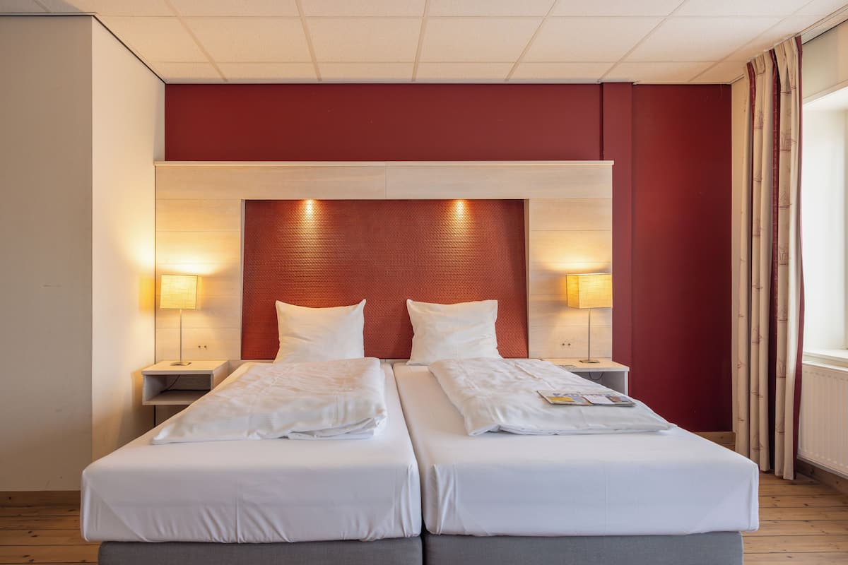 Une chambre double avec deux lits, chacun doté de draps et d’oreillers blancs, d’un mur d’accent rouge et de deux lampes de chevet.