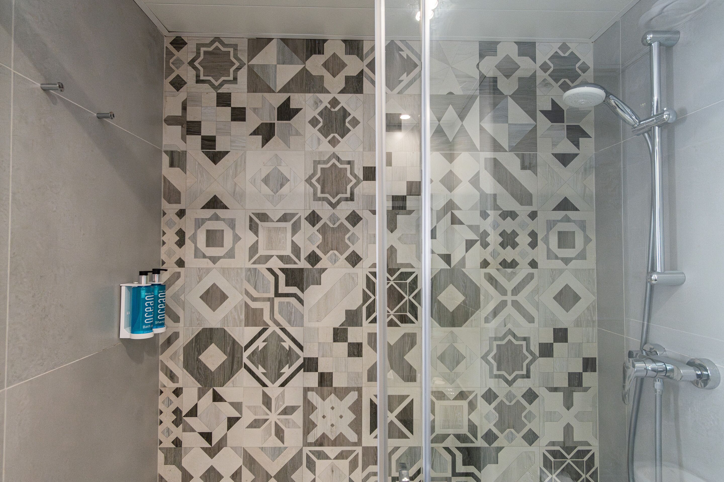 Area doccia con parete rivestita in piastrelle decorate, box doccia in vetro e soffione a mano.