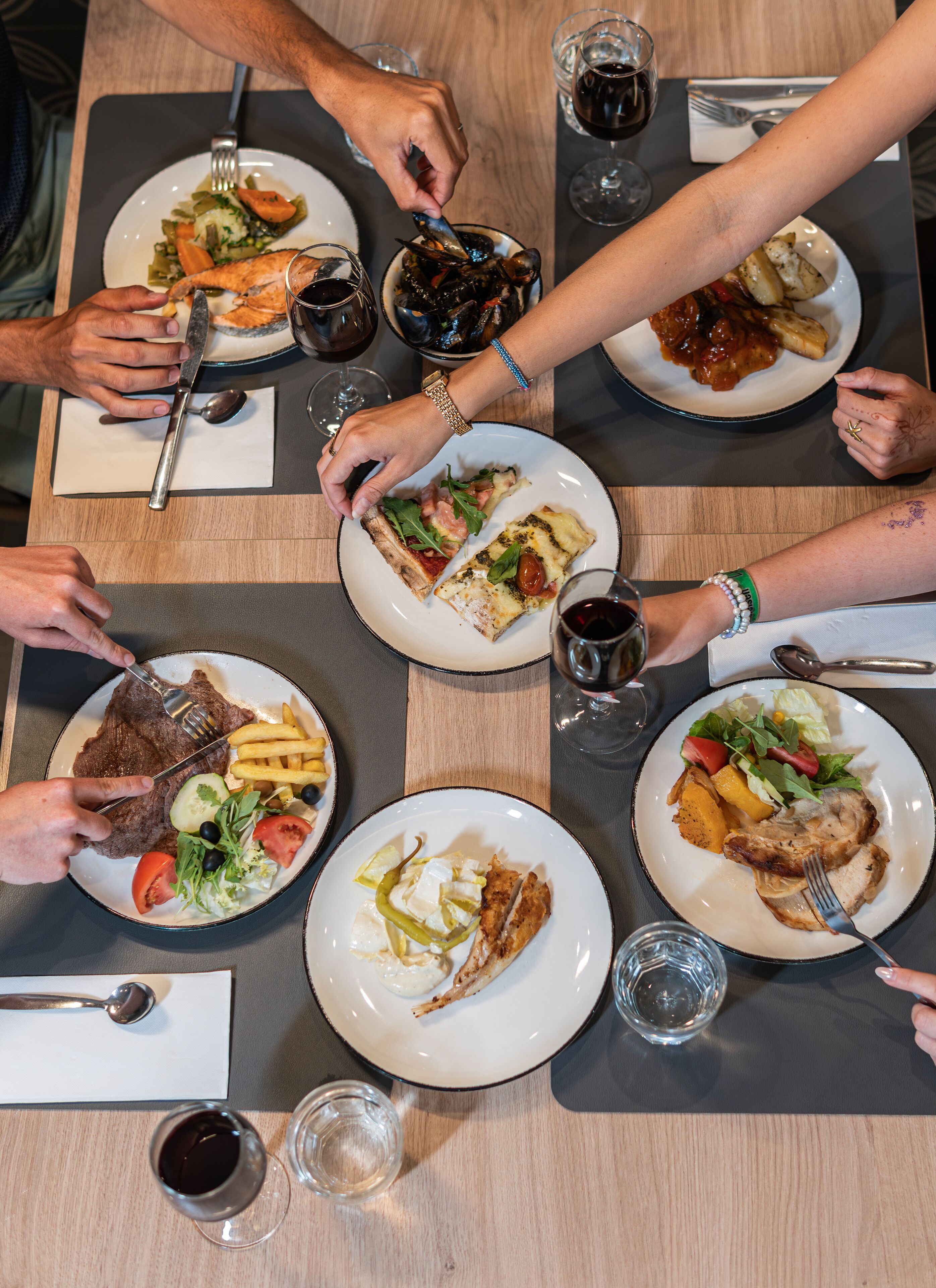 Eine Gruppe von Personen speist an einem Tisch mit verschiedenen Gerichten, darunter Steak, Pommes und Salate.
