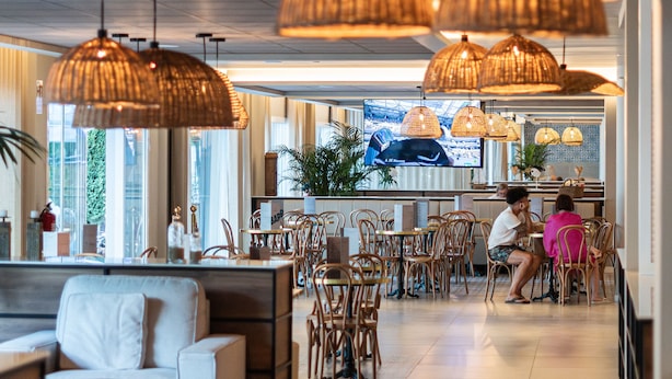 Un restaurante moderno con lámparas colgantes de mimbre, un sofá y una pantalla de televisión al fondo.