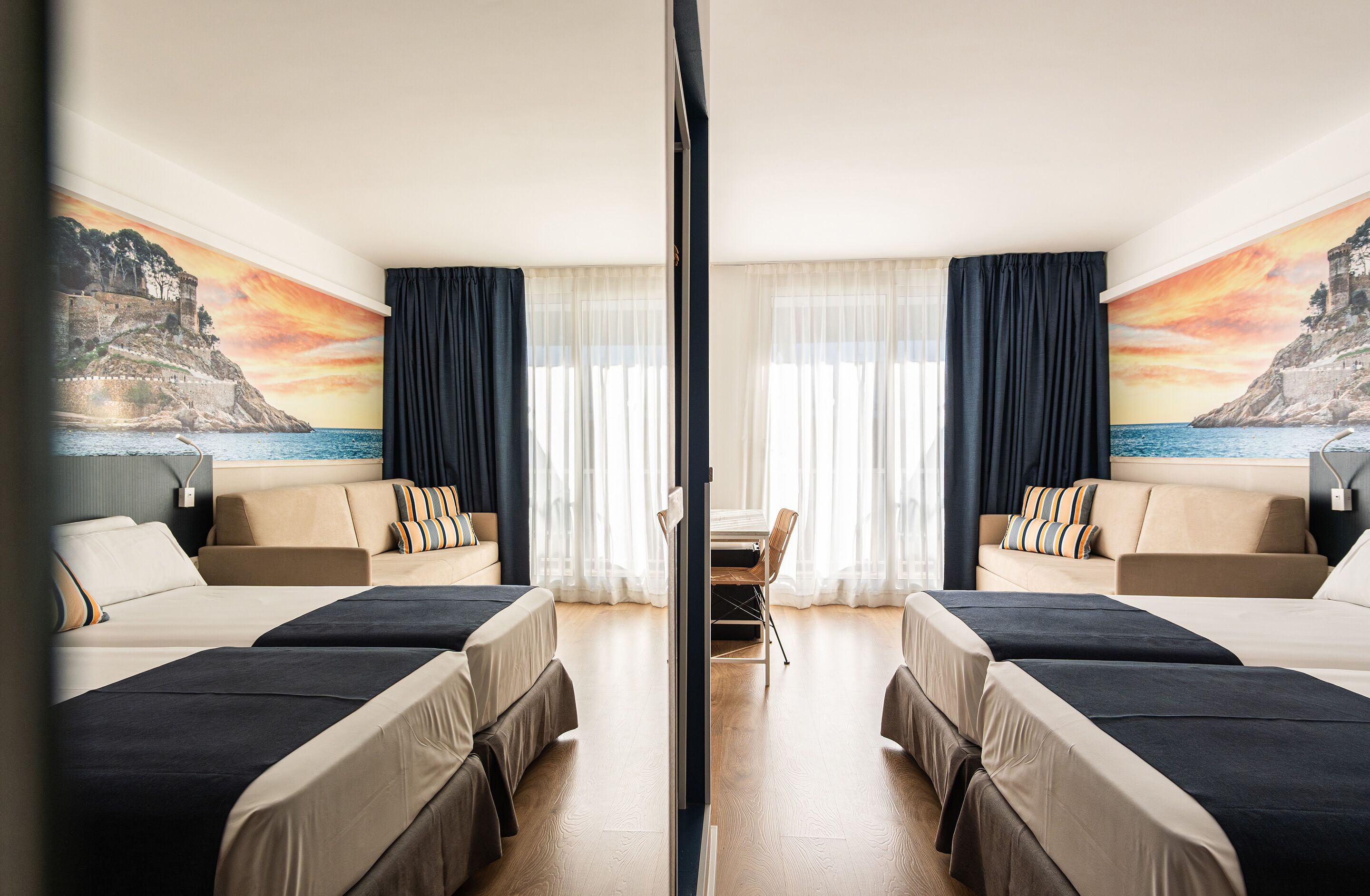 Habitación de hotel con dos camas, un sofá, una mesa de comedor y vistas a un paisaje costero.