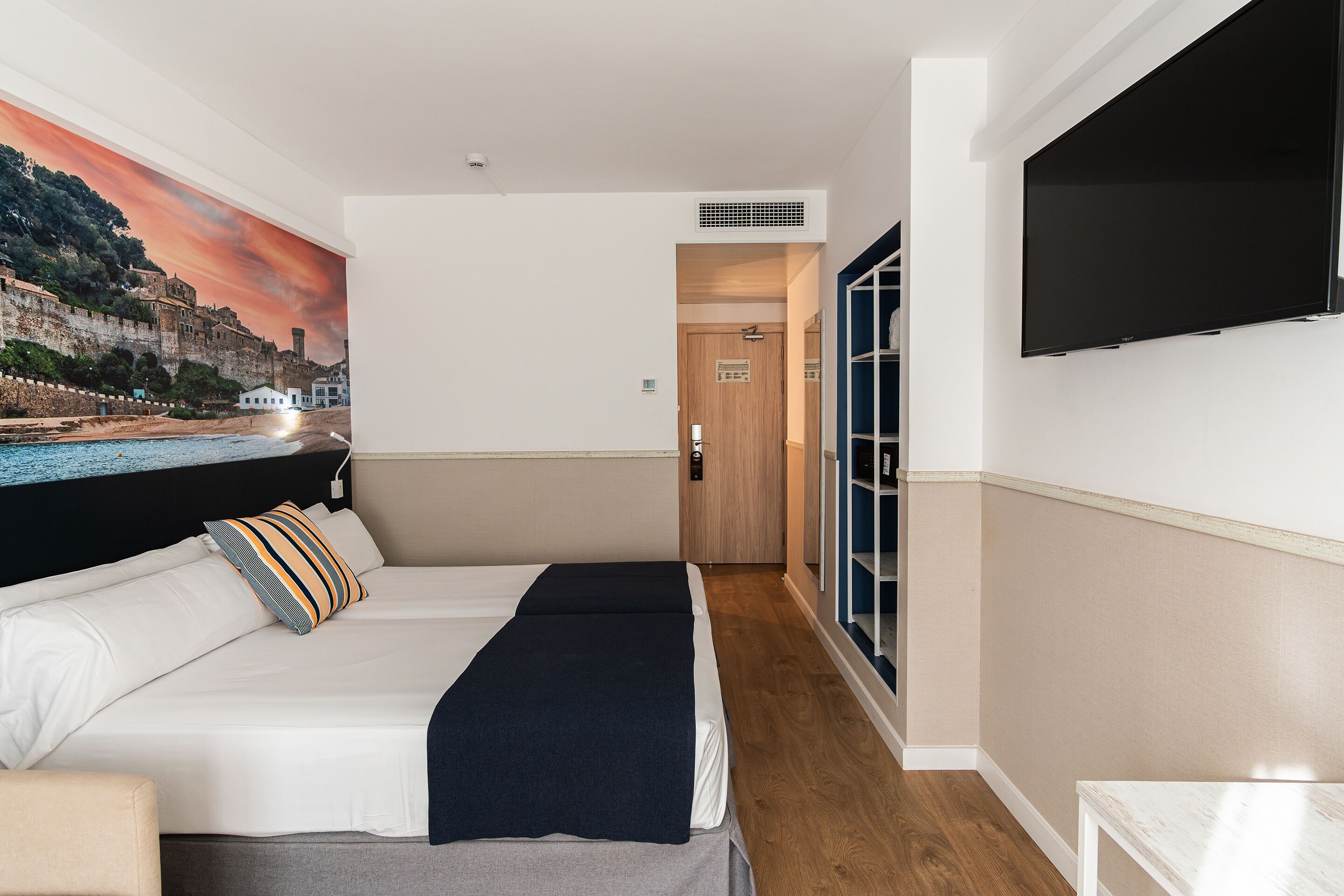 Habitación de hotel con cama, televisor, un cuadro de una escena costera y suelo de madera.