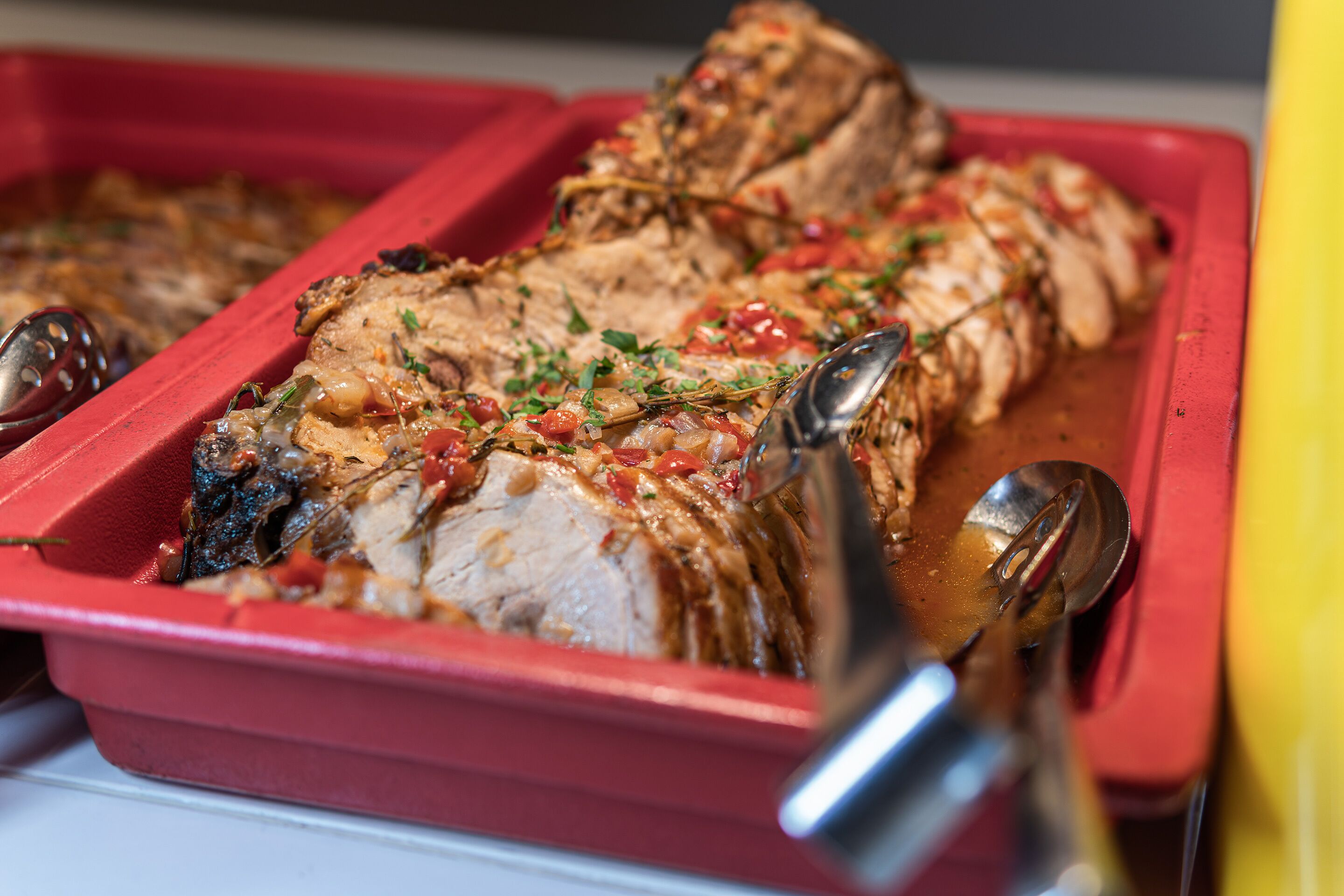 Un plat de service rouge contenant de la viande coupée en tranches, garnie d’herbes et de tomates.