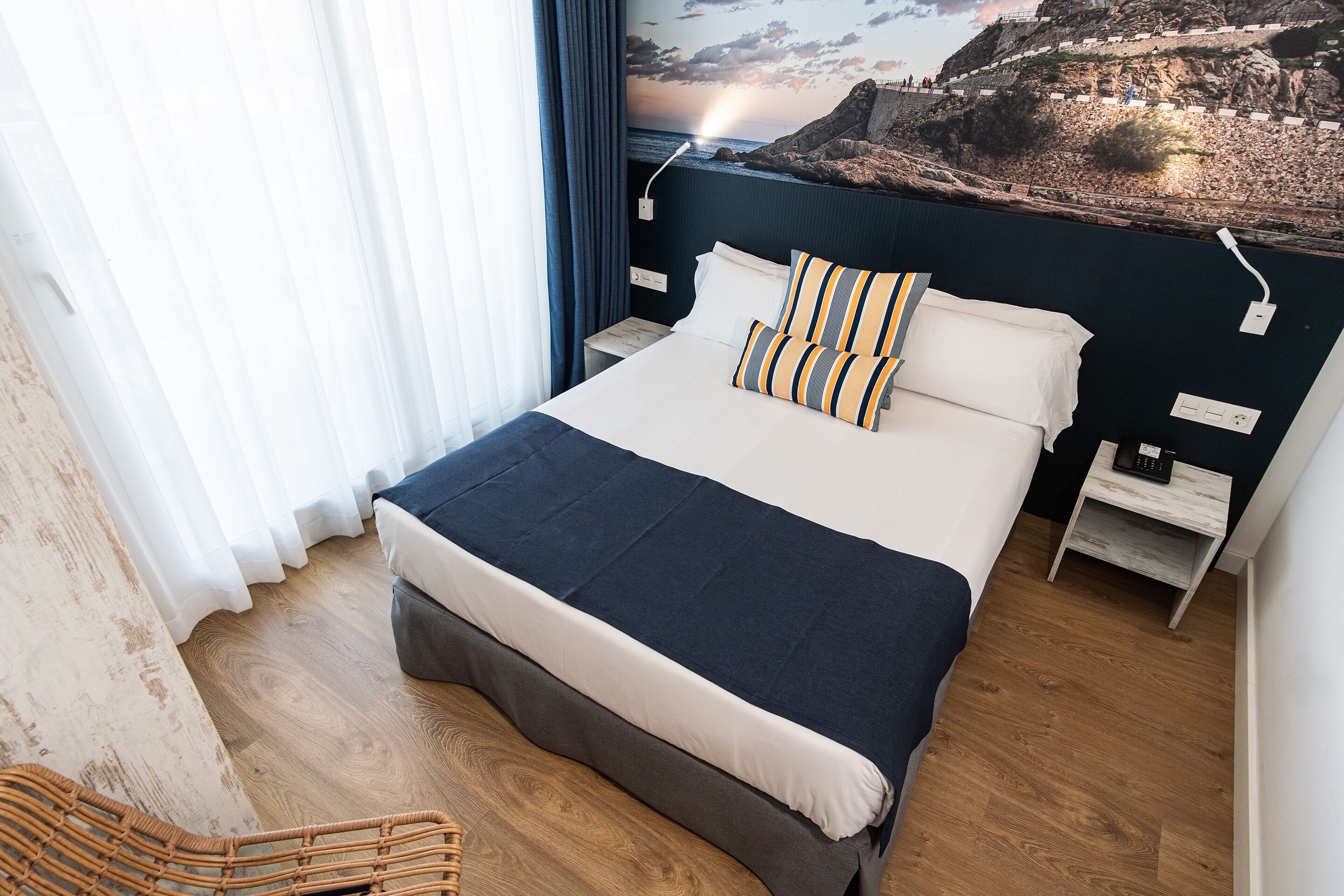 Een net opgemaakt bed met een donkerblauwe en witte sprei, twee kussens en een nachtkastje met een lamp.
