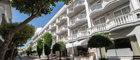 A hotel with multiple balconies, outdoor seating, and a tree-lined street.