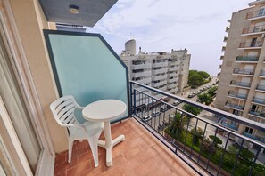 Un balcón con mesa y sillas, que da a una vista urbana con edificios y una calle.