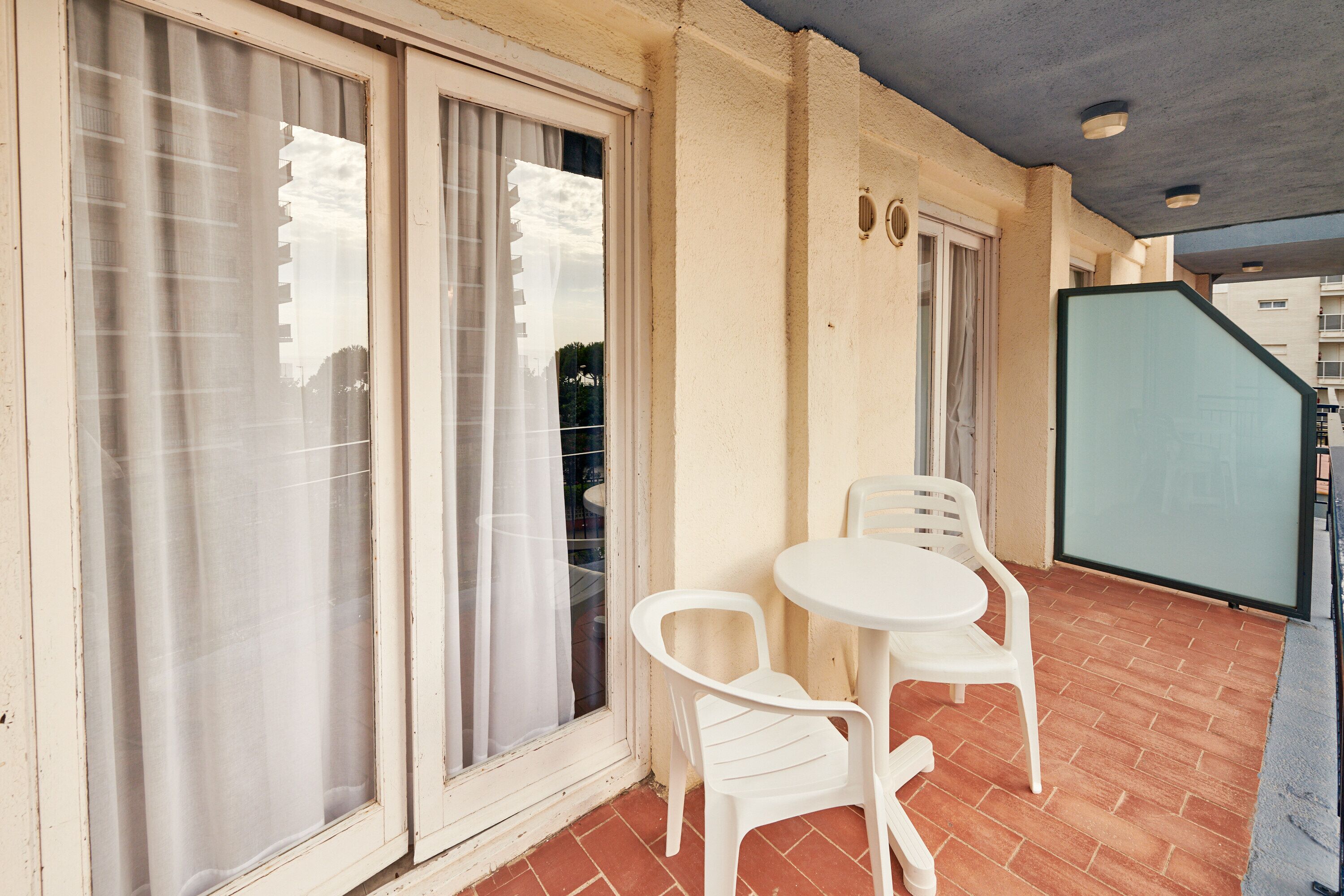 A balcony with a table and chairs, a sliding glass door, and a view of a building in the background.