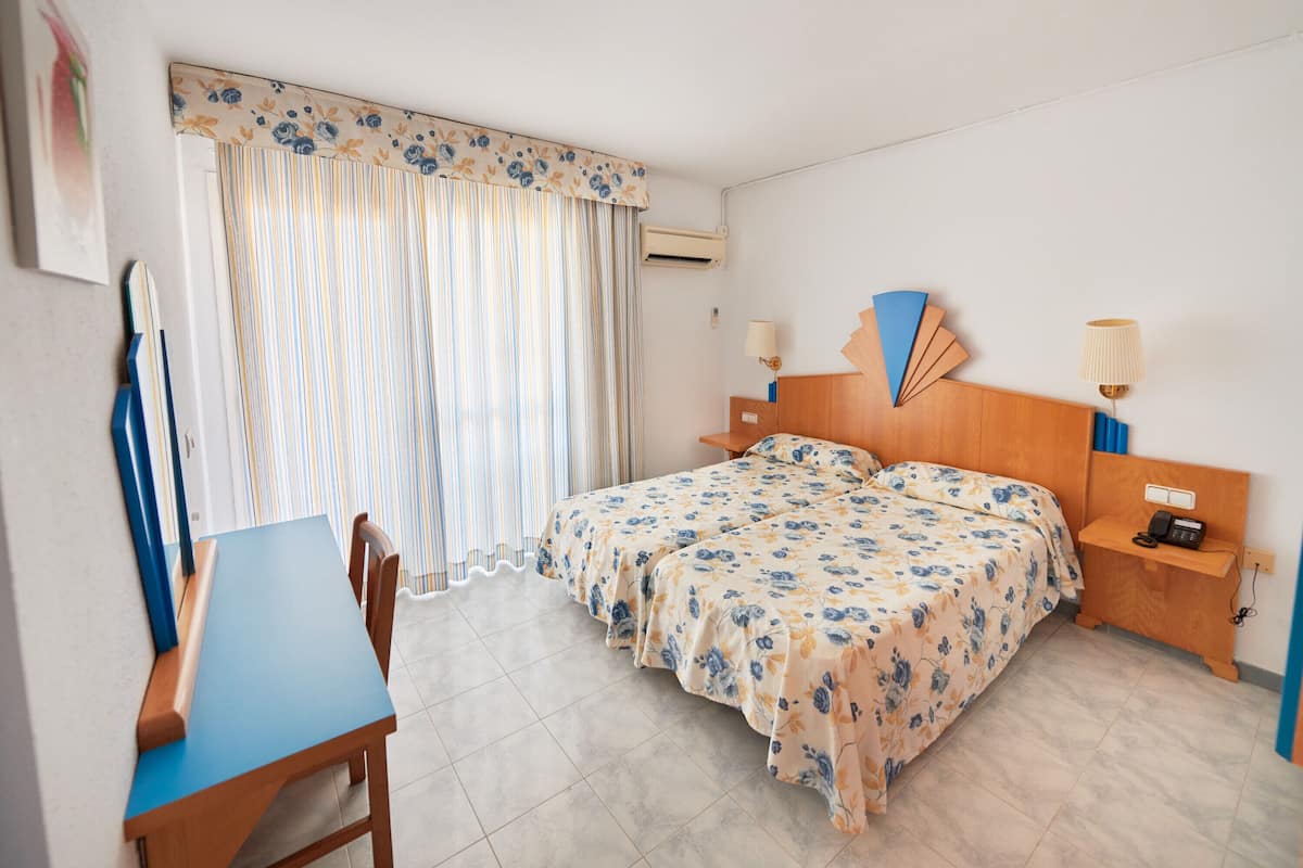 Una habitación de hotel con una cama, mesitas de noche, un escritorio y una silla.