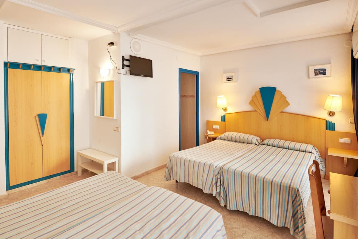 Habitación de hotel con dos camas, un armario de madera, una mesita de noche pequeña, un escritorio y una silla.