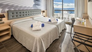 Habitación de hotel con dos camas, un escritorio, una silla y vista al océano.